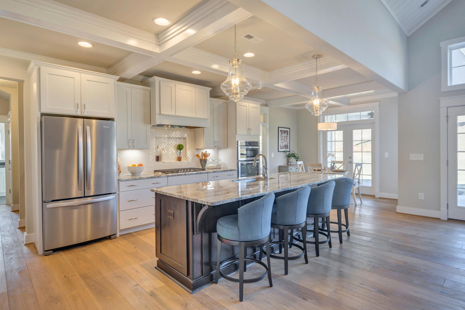Craig Builders open kitchen in Oak Hill Farm. An elegant kitchen island with a built-in sink is situated beneath pendant lighting.